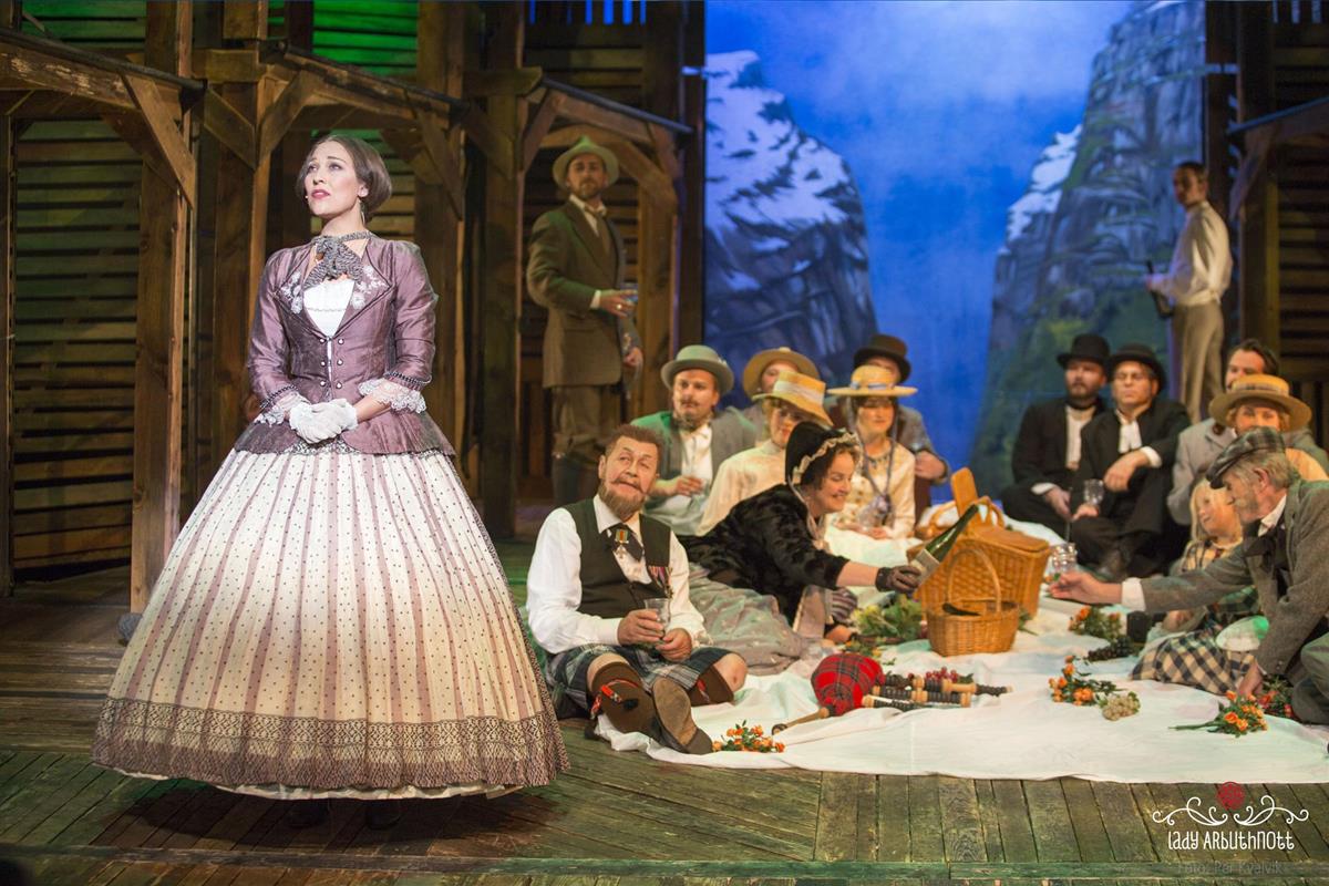 scene fra musikkspillet, med hovedpersonen lady Arbutnott i forgrunnen og flere "engelskmenn" i bakgrunnen, ute på piknik i kulisser av sunndalsfjell - Klikk for stort bilde