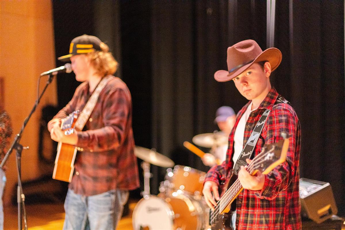 Band spiller musikk med kassegitar, bass og trommer på en scene - Klikk for stort bilde